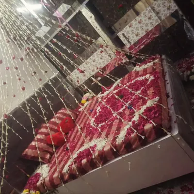 This bridal room decoration features a bed covered in a pattern of red and white rose petals. Hanging strings of jasmine and rose flowers create a beautiful floral curtain effect from the ceiling.
