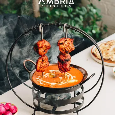 This is our Signature Butter Chicken, presented with theatrical flair. We serve the smoky, tandoor-grilled chicken on skewers over a velvety, slow-cooked tomato-butter gravy, creating a dish that is an experience in itself.