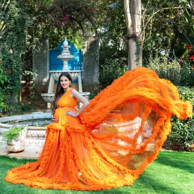 A stunning portrait of a mom-to-be in our vibrant orange ruffled gown, with the fabric creating a beautiful flying effect. This was taken in a garden with a classic fountain, adding a touch of elegance.