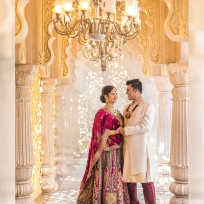 A truly regal portrait of a couple in a grand, pillared hallway. The intricate architecture and warm chandelier light create a majestic atmosphere, perfect for a royal-themed pre-wedding shoot.