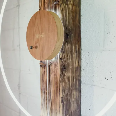 The STORY clock mounted on a rustic wooden beam against a white brick wall. This demonstrates its versatility as a wall clock that blends natural materials with futuristic time-telling.