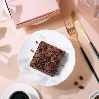 A top-down shot of a rich chocolate brownie from Manam Chocolate, paired with black coffee. This clean, bright styling is perfect for social media and menu photography.