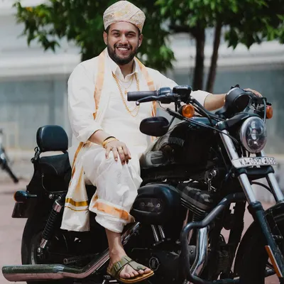 The groom, looking dapper in his traditional attire, poses with a Harley Davidson, blending tradition with a cool, modern edge.