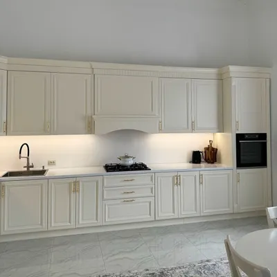 A beautiful, expansive kitchen in a classic off-white finish. The moulded cabinet doors, elegant gold handles, and integrated range hood cover create a seamless and timeless look of luxury.