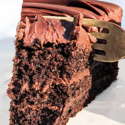 This is what real chocolate cake looks like. A fork sinking into the moist crumb and velvety ganache of our Belgian Dark Chocolate cake, made with real cocoa beans.