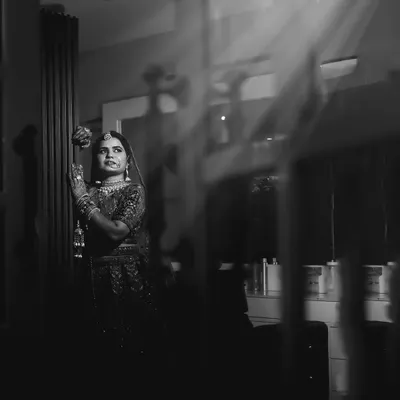 A moody and artistic black and white bridal portrait. The bride is captured through a reflection, with dramatic light and shadows creating a sense of quiet contemplation and timeless elegance.