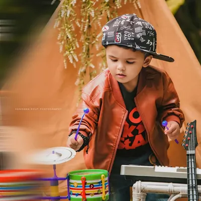 This little rockstar is ready for his concert. With a toy drum set, keyboard, and a cool leather jacket, this themed toddler photoshoot captures a fun and energetic performance.