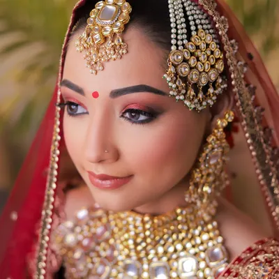 A quintessential bridal portrait focusing on flawless HD makeup. The model's red eyeshadow and defined features are perfectly complemented by heavy kundan jewellery against a traditional red bridal dupatta, creating a classic and aspirational look for any MUA's portfolio.