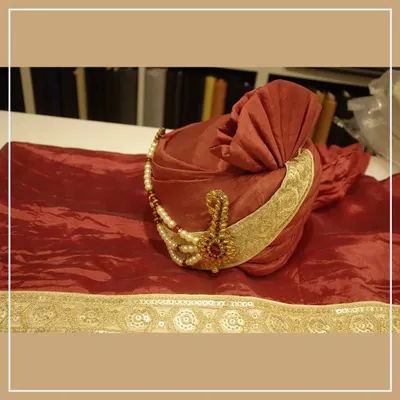 A beautiful red groom's pagri (turban) with a gold border and a traditional sarpech (turban ornament). This is a key accessory for a royal wedding look.