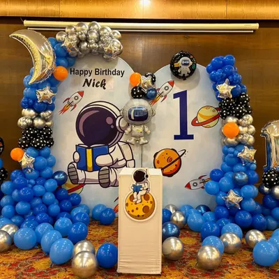 We created an out-of-this-world astronaut theme for Nick's first birthday. The decor includes a custom space backdrop, balloon columns in blue, silver, and black, and special foil balloons like a crescent moon and an astronaut.