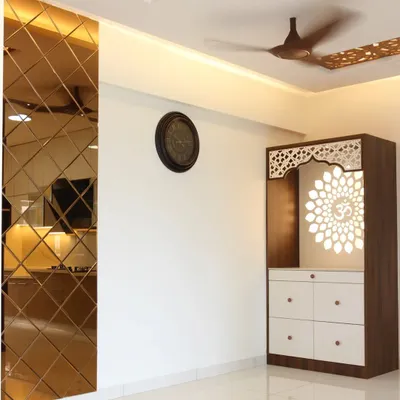 A beautiful free-standing pooja unit with a backlit 'Om' mandala cut into a jali panel. The design is framed by a bronze mirror accent wall and intricate CNC work on the ceiling.