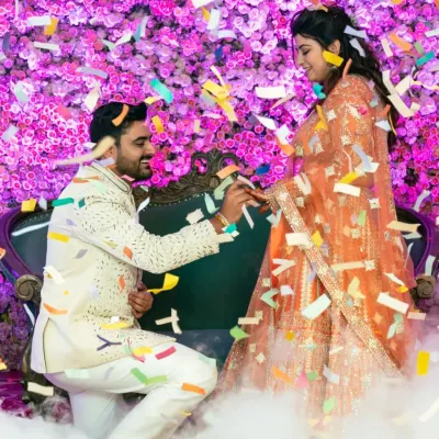 A picture perfect engagement moment. The groom is on one knee, surrounded by a cloud of smoke and a shower of confetti, against a stunning floral backdrop.