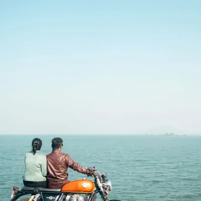 Two adventurers looking out at the horizon, seated on their Royal Enfield. This shot captures the promise of the open road and a life of shared journeys by the sea.