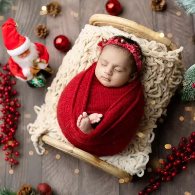 A festive Christmas-themed newborn shoot. A baby swaddled in red on a tiny sleigh, surrounded by ornaments and a miniature Santa, makes for the perfect holiday card.