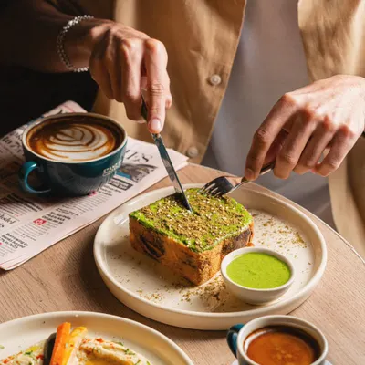 This shot for Stand By Coffee captures food in the context of a meal. The hands cutting into the toast, the latte art in the coffee, and the newspaper on the table create a complete lifestyle scene that feels authentic and inviting.