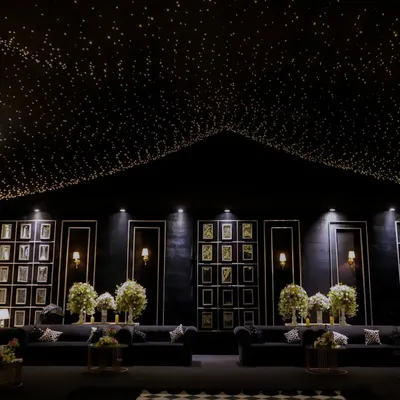 A wide view of a modern monochrome lounge we designed. A ceiling of countless fairy lights creates a starry night effect above a chic black seating area with a gallery wall, perfect for a sophisticated corporate mixer.