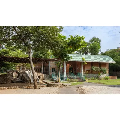 The entrance to the Foothill Learning Centre is designed to be welcoming and integrated with nature. The structure combines rammed earth walls, a green roof, and an open play area, immediately establishing a connection to the outdoors.