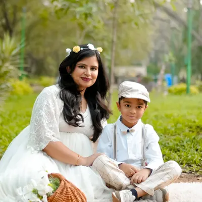 A mother and son enjoying a peaceful moment together during an outdoor picnic-style photoshoot. The natural light and green surroundings create a soft and serene family portrait.