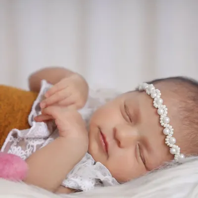 A detailed close-up shot allows us to capture the serene expression of a sleeping newborn. The delicate lace outfit and pearl headband add a touch of elegance without distracting from the baby's natural beauty.