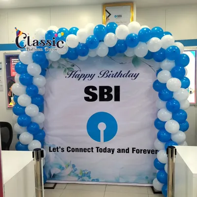 A branded "Happy Birthday SBI" backdrop framed by a blue and white balloon arch inside a bank branch. This setup is ideal for celebrating corporate anniversaries and milestones right where your customers are.