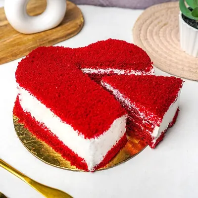 A vibrant heart-shaped red velvet cake with a slice cut out, shot on a clean, bright background.