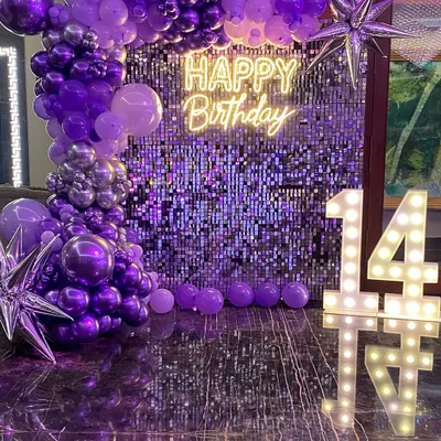 A glamorous 14th birthday setup with a purple shimmer wall. This decoration features a stunning organic balloon garland in shades of purple and silver, a 'Happy Birthday' neon sign, and large marquee numbers.