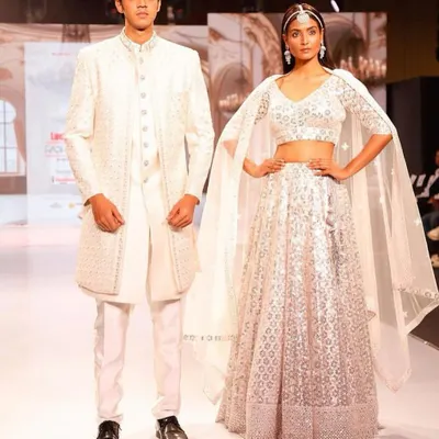 A stunning couple on the runway showcasing our coordinated white collection. The groom's sherwani and bride's lehenga feature matching embroidery, creating a look of pure elegance.