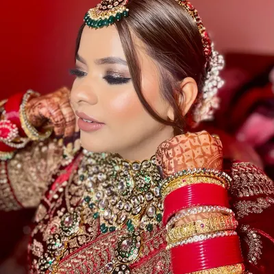 A close-up of this royal bridal look. I created sharply defined, smokey eyes with a touch of glitter and a soft nude lip to perfectly balance the richness of her red velvet lehenga and green jewellery.