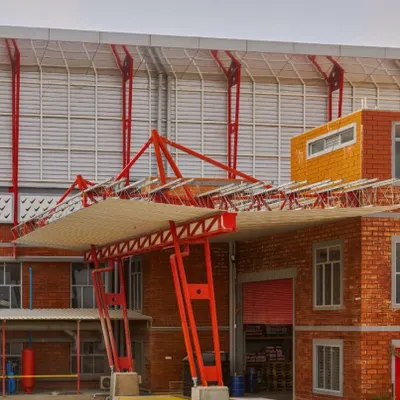 The loading bay of the Varna Paint Factory in Dobbespet, completed in 2017. This image highlights our approach to industrial architecture, where functionality is expressed through bold design. The prominent red structural steel frame contrasts with the exposed brickwork, creating a strong visual identity for a heavy-duty workspace.