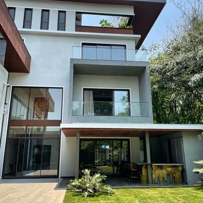 The design for this Koramangala residence features expansive glass, multiple balconies, and a seamless connection to the outdoor lawn and bar area, perfect for modern living.