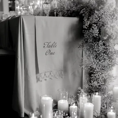 My basics are clear, no basic please. This black and white shot highlights the clean lines and sophisticated details of an all-white tablescape, featuring a cascade of baby's breath and an abundance of candles.