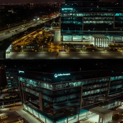 A dramatic night-time aerial shot of the Collins Aerospace building in Bengaluru. Our low-light drone photography highlights the building's modern design and illumination against the city skyline.