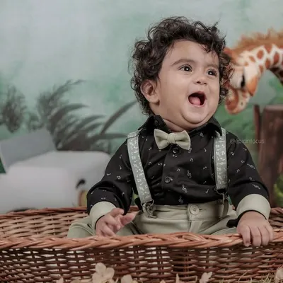 This little explorer, dressed in a bow tie and suspenders, looks up with excitement in our jungle-themed setup, complete with a friendly giraffe prop.