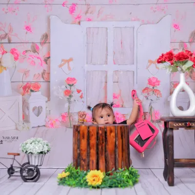 A peek-a-boo moment from inside a rustic prop. This playful shot in our floral garden setup adds an element of surprise and fun to the baby girl's photoshoot.