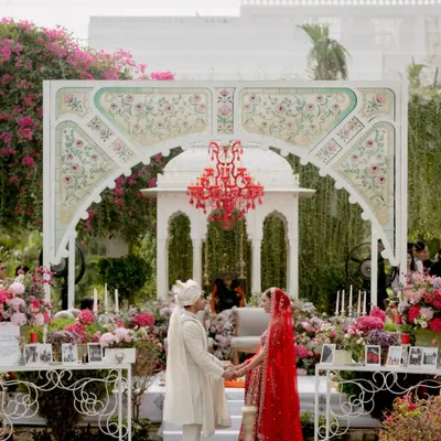 A full view of the hand-painted mandap backdrop we created for Sarah and Vikram's "Tale as Old as Time" wedding. The stunning red chandelier served as the focal point, surrounded by a garden of pink and red florals.