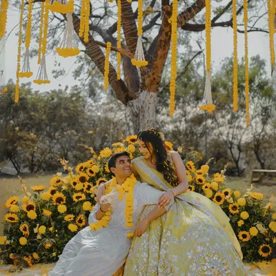 A dreamy Haldi setup under a tree, with hanging marigold garlands and a seating area nestled in a bed of sunflowers. This is how we turn a traditional ceremony into a fairytale moment.