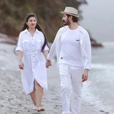 A candid walking shot on the sandy banks of the Ganga. The couple is dressed in white, creating a clean and serene look that complements the natural surroundings.