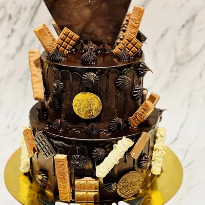 A two-tier chocolate overloaded cake for Trisha. This ultimate indulgence is covered in chocolate ganache and decorated with a variety of chocolate bars like KitKat and Dairy Milk.