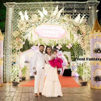 A breathtaking entrance to Varnnika's fairyland, featuring two large castle turrets and an ornate archway decorated with flowers. The family stands together, ready to welcome guests to the royal celebration.