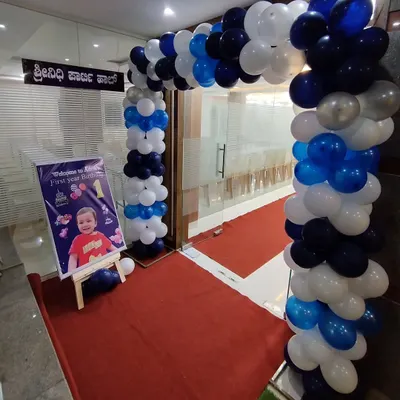 A classic blue, white, and silver balloon arch creating an inviting entrance for a first birthday party. A personalized welcome sign is placed at the entrance.