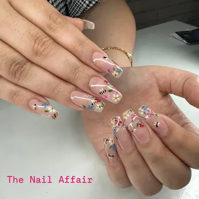 An intricate, hand-painted floral design on long, clear square extensions. This 'meadow' look features tiny flowers and bees for a whimsical, detailed finish.
