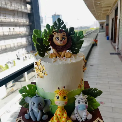 A delightful jungle safari cake featuring a fondant lion, elephant, giraffe, and zebra. The cake is decorated with lush green leaves and touches of gold leaf for a hint of wild elegance.