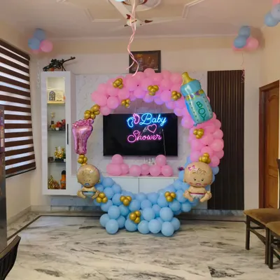 A classic baby shower decoration for a home setting. I created a balloon ring with pink and blue sections, a 'Baby Shower' neon sign, and themed foil balloons like a baby bottle and foot.