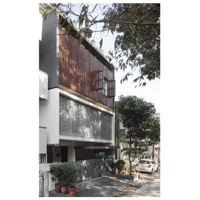 The '10 x 10 Residence' stands on a compact 30x30 feet plot in a dense urban area. The facade is a study in contrasts, with a solid, textured 'jaali' screen on the first floor and a lighter, slatted wooden screen on the second.