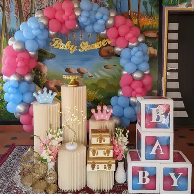 A fun and modern baby shower decor for a gender reveal party. The setup includes a pink and blue balloon arch, "BABY" blocks, and decorative pedestals with props.