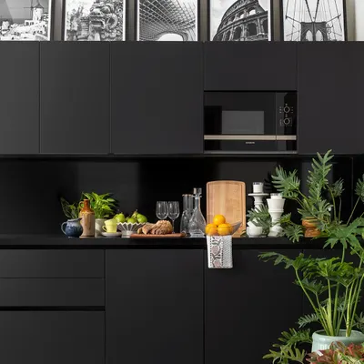 A sleek and moody all-black kitchenette in the Juneja Residence. The minimalist, handle-less cabinets create a seamless look, while the black-and-white architectural photographs above add a personal and artistic touch.