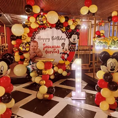 A classic Mickey Mouse theme for a memorable first birthday. This setup at BBQ Company, Rajouri Garden, includes a full balloon arch, character cutouts, and a large light-up number '1' for the perfect photo backdrop.