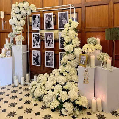 For a 30th anniversary, we created this elegant memory wall. A cascade of white hydrangeas frames a collection of the couple's photos, creating a beautiful and sentimental focal point grounded by the warm glow of candles.