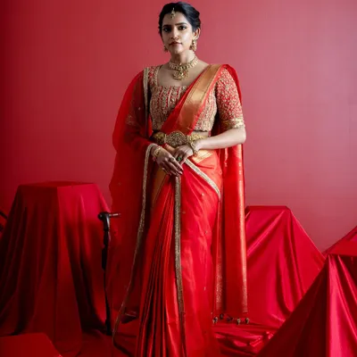 A full-length portrait of a bride in a classic red and gold Kanjeevaram saree. Paired with a heavily embroidered custom blouse and traditional temple jewelry, this look embodies the grace and grandeur of a South Indian wedding ceremony.