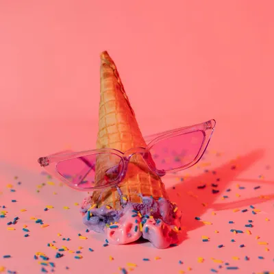 This fun, conceptual photo for an eyewear brand features pink sunglasses on a melting ice cream cone. The vibrant pink lighting and colorful sprinkles create a playful and summery image that is sure to grab attention.